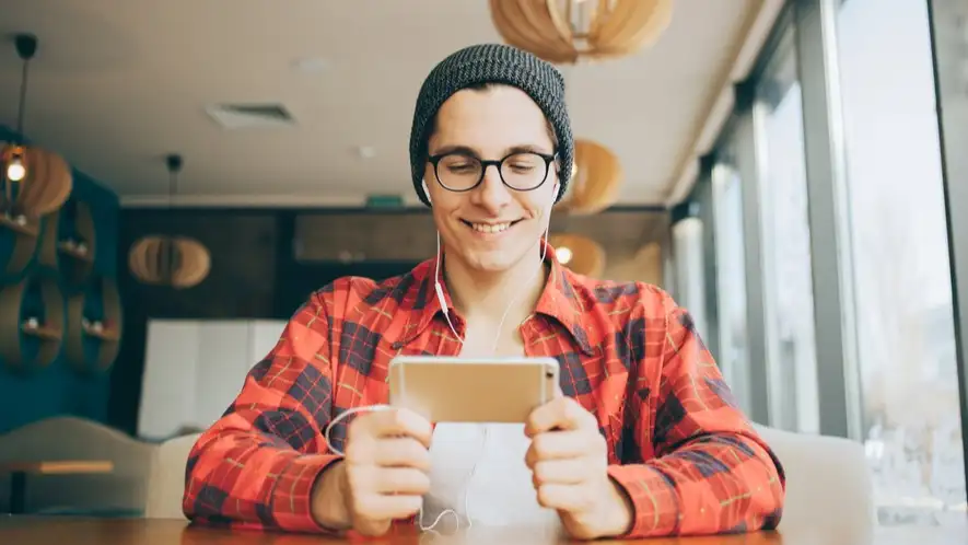 Young man sitting in office,holding a mobile phone and watching video - 8 Video Editing Tips to Keep Viewers Engaged - Clipchamp Blog
