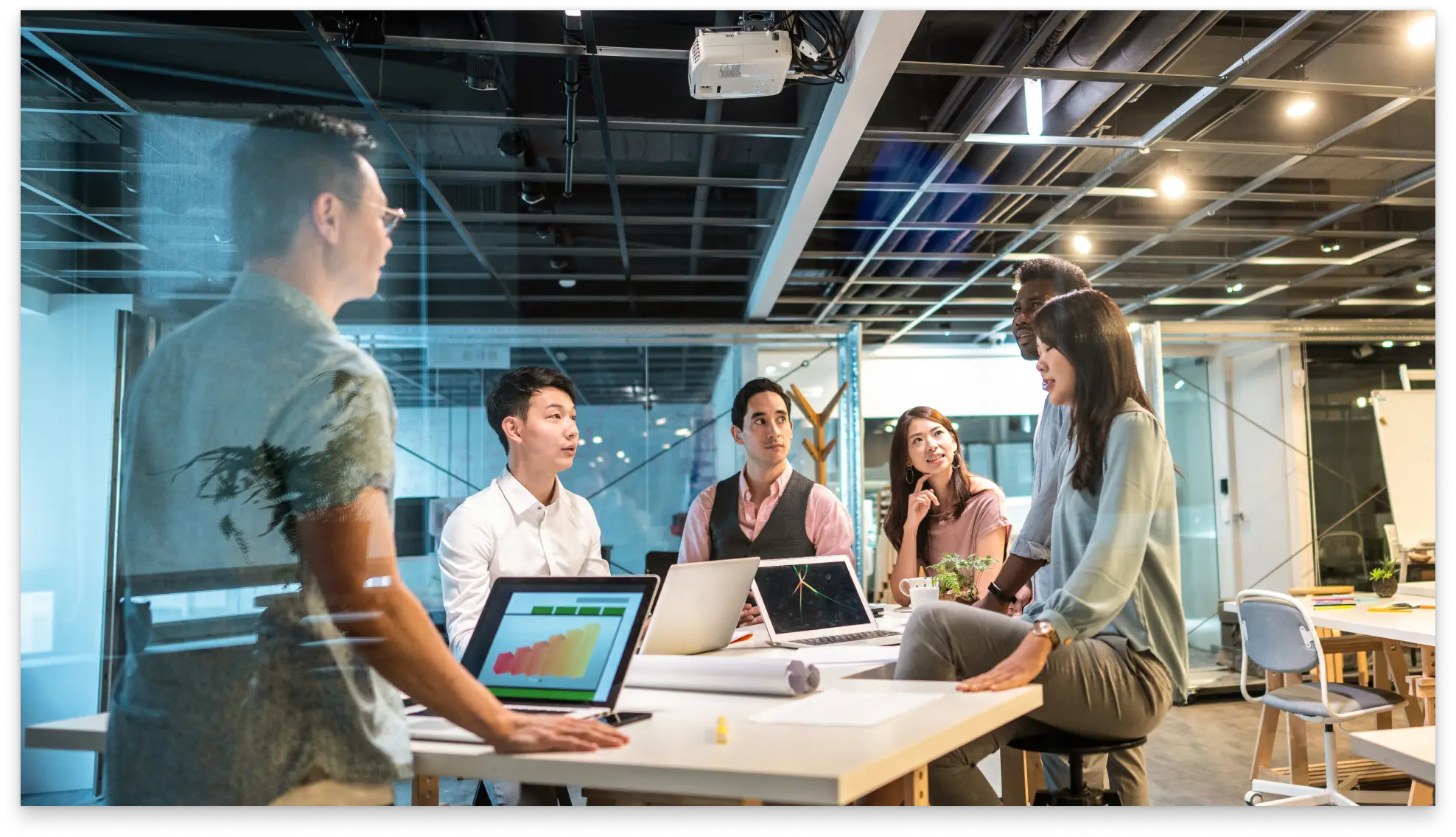 Team of professionals collaborating in an office environment with laptops and shared screens
