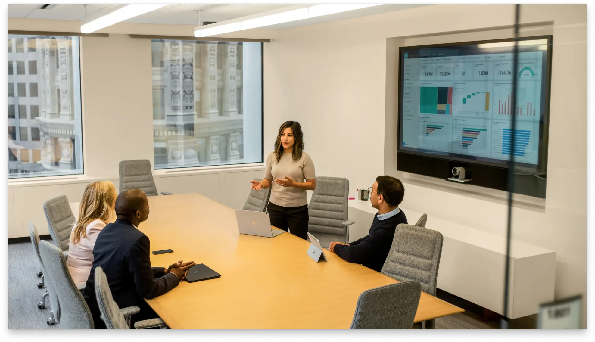 Four people in a meeting room reviewing financial data on a large screen.