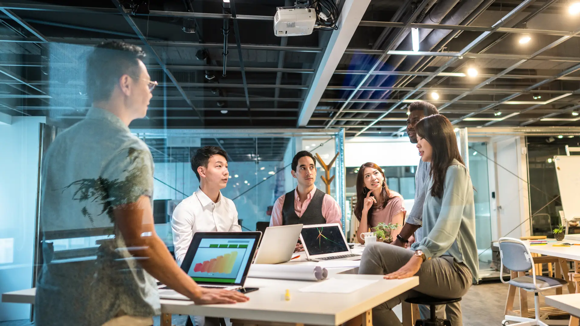 A group of office workers gathered around discussing a spreadsheet as a team.