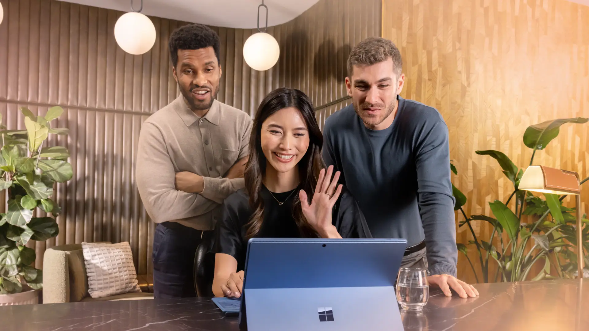 A woman and two men smiling and waving at a computer screen.