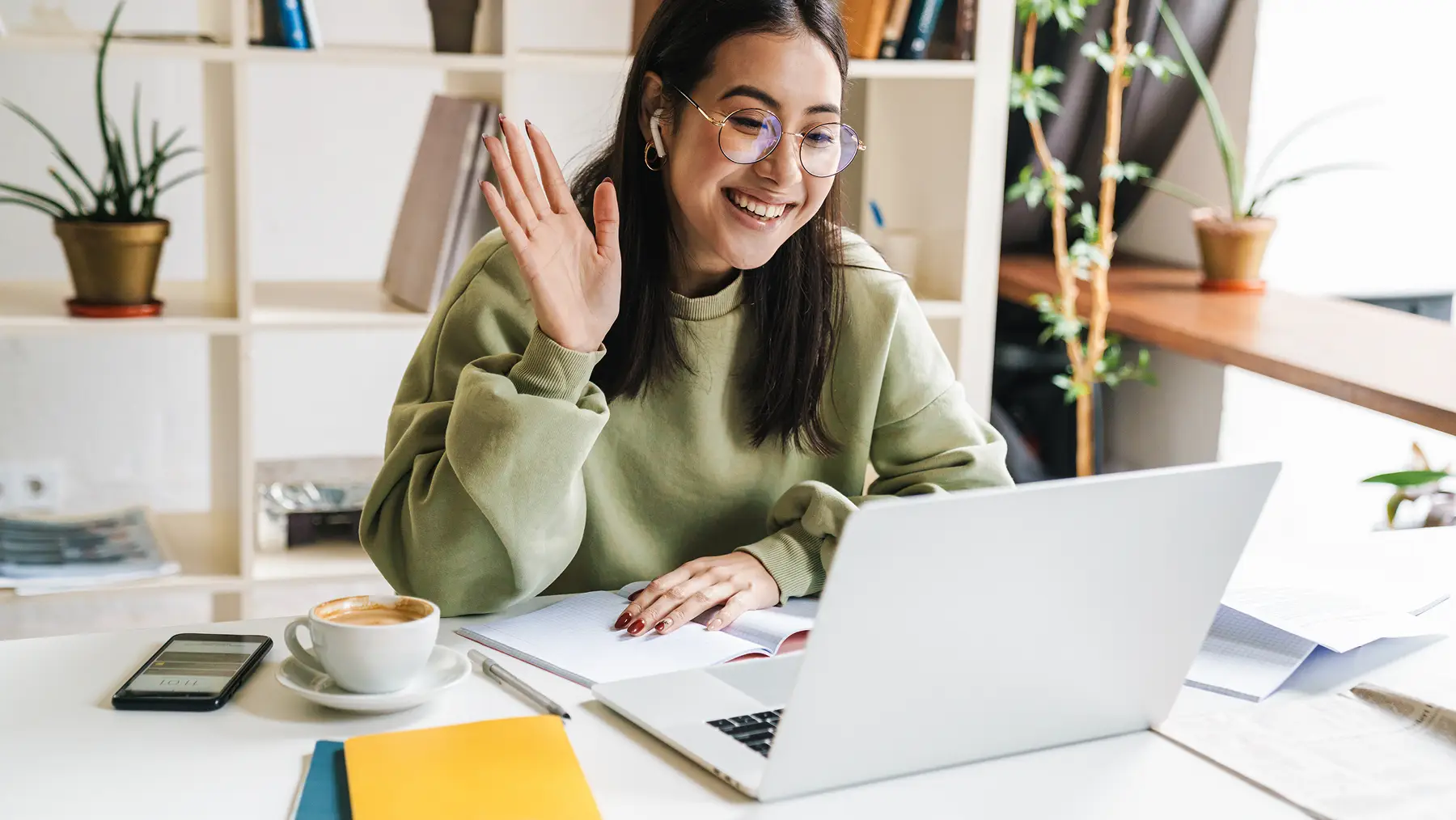 A woman waving to her laptop at a desk